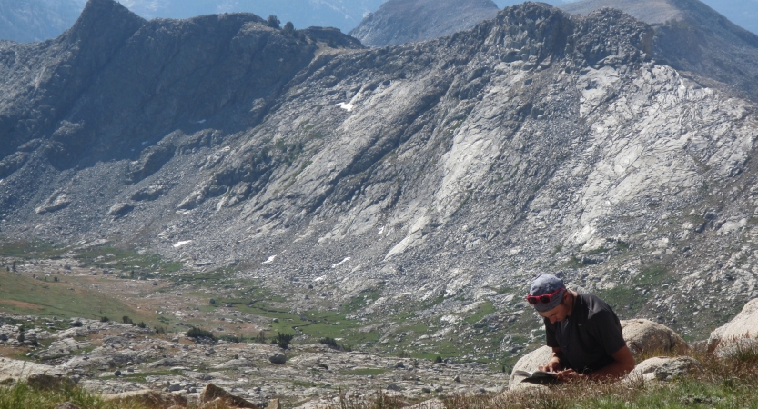 A person sits on a rock journaling above a vast mountain landscape. 